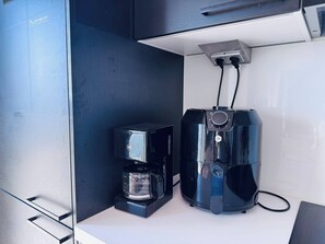 A kitchenette with a coffee maker and a coffee pot, both black, and a power outlet above them. - Nordic Home Bliss With Sports (Helsinki)