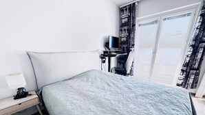 Quarto de hotel com cama, escrivaninha, cadeira, televisão e janela com cortinas.