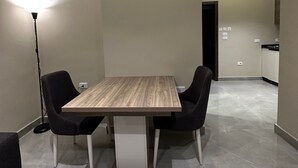 A modern dining area with a wooden table and black chairs, a floor lamp, and a kitchen in the background. - 304 Al-najeh JRE Apartments For Rent ave (Amman)