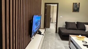 A modern living room with a flat-screen TV, a sofa, a coffee table, and a wooden slatted wall. - 304 Al-najeh JRE Apartments For Rent ave (Amman)