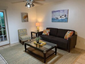 Ein Wohnzimmer mit Sofa, Sessel, Couchtisch, Lampe und Kunstwerken an den Wänden.