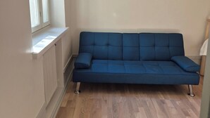 A room with a blue sofa, a radiator, a window, and wooden flooring.