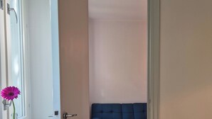A doorway leading to a room with a blue sofa and a window with a flower vase.