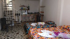 Une chambre avec une couvre-lit à motifs, une chaise, un bureau avec une autre chaise, un petit coin cuisine et un escalier en colimaçon.