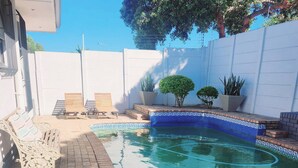 En swimmingpool med en blå mosaikbård, omgiven av en vit mur och planterade blommor i krukor.