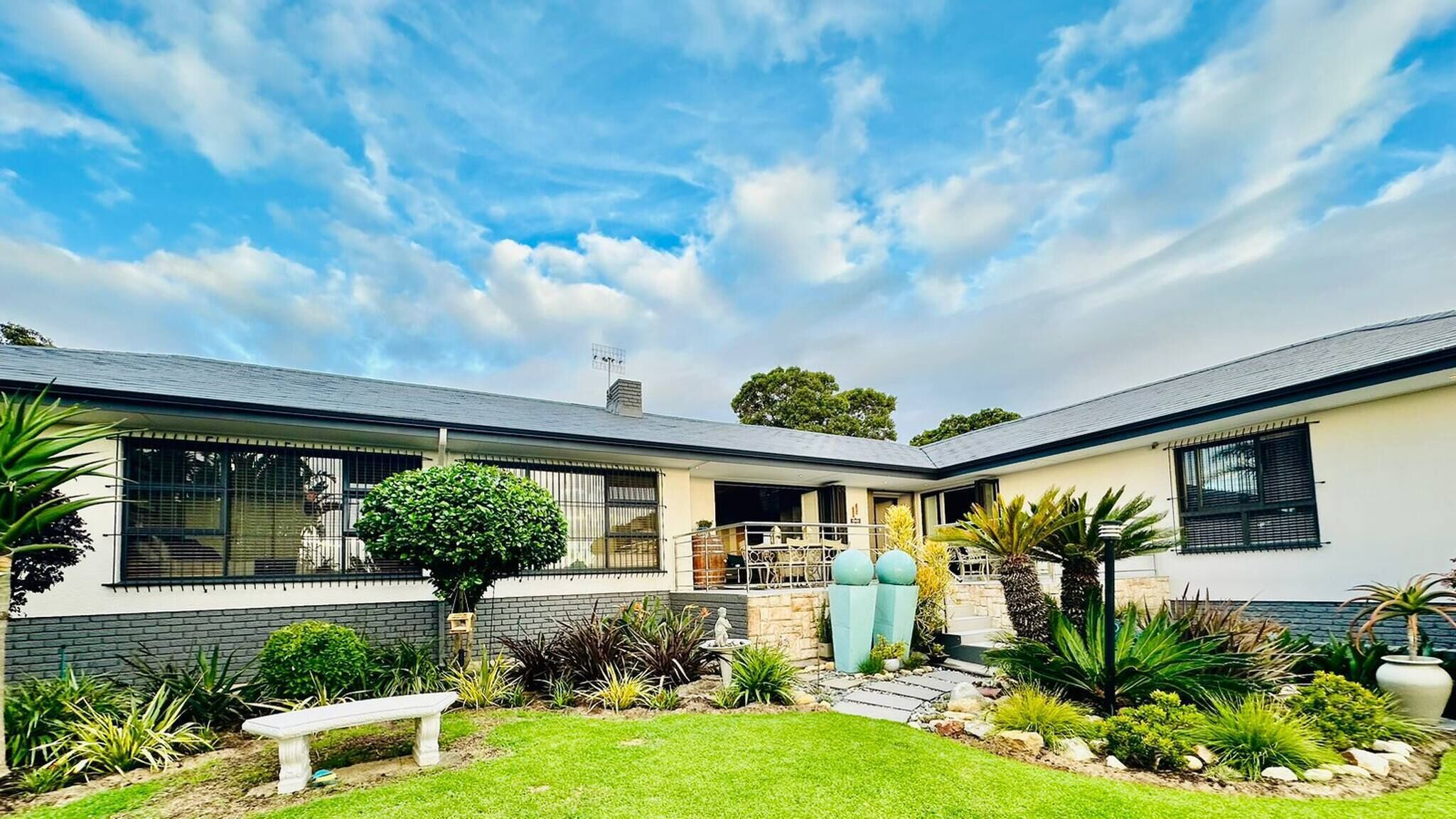 A modern two-story house with a covered patio, a well-maintained garden, and a clear sky.