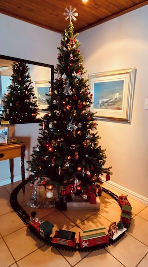A decorated Christmas tree with ornaments and lights, surrounded by a train set on a tiled floor. - Bonita Vista Plattekloof (Cape Town)