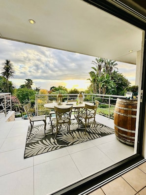 A balcony with a table and chairs, a large barrel, and a view of the sunset. - Bonita Vista Plattekloof (Cape Town)