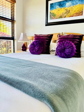 A neatly made bed with a grey blanket, two purple pillows, and a painting of a landscape above it. - Bonita Vista Plattekloof (Cape Town)