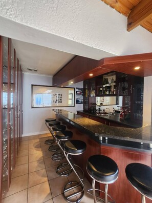 Una zona de bar con una barra alargada, varios taburetes y una exhibición de botellas.