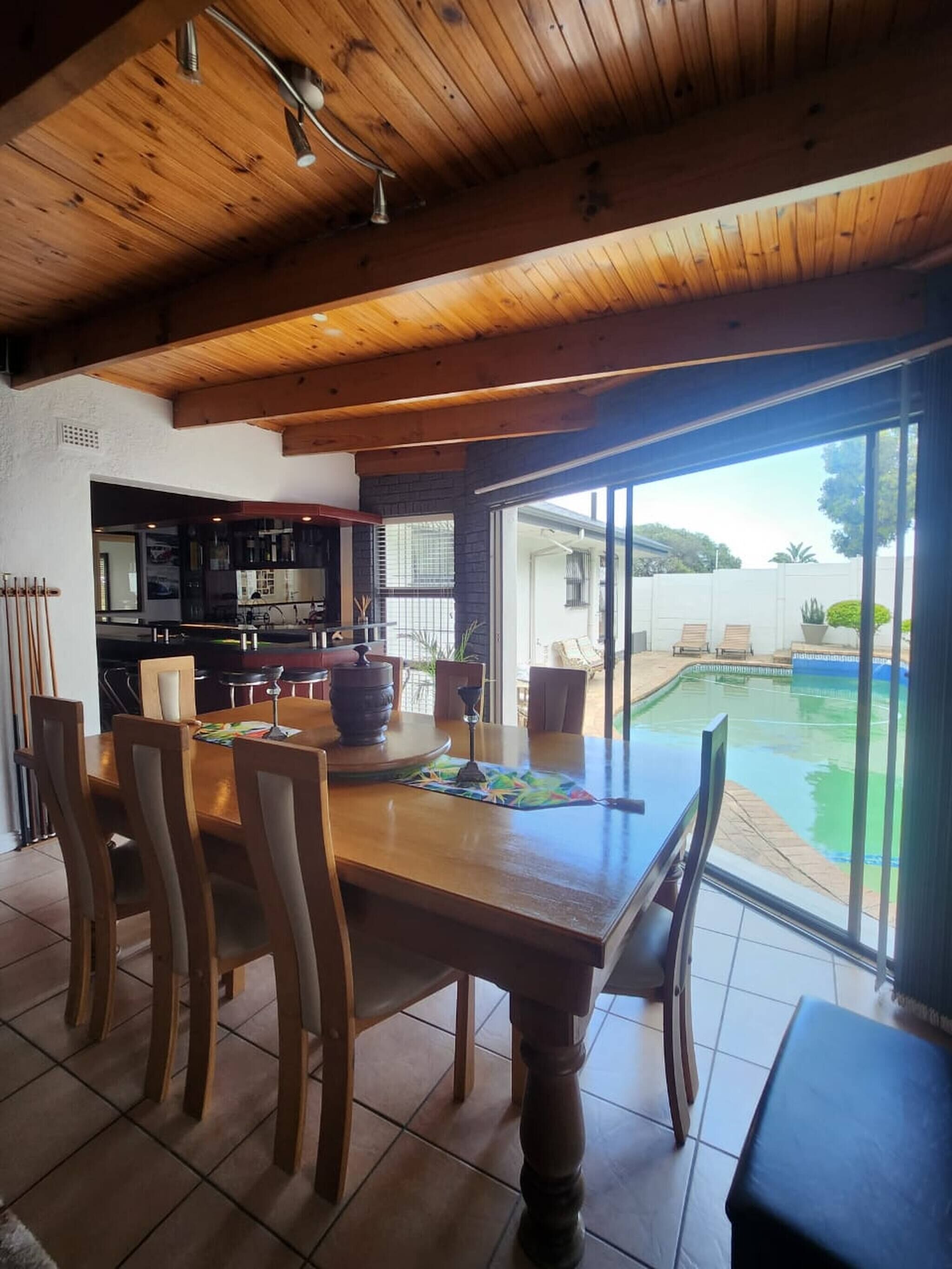 Een eethoek met een houten tafel en stoelen, een keuken op de achtergrond en uitzicht op een zwembad buiten.