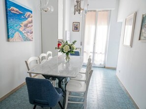 A dining area with a marble table, white chairs, a vase with flowers, and a painting on the wall. - Modern Apartment Near Senigallia's Velvet Beach (Senigallia)