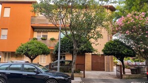 A residential street with a black car parked on the side, a tree in the foreground, and a building with a brown door and windows. - Modern Apartment Near Senigallia's Velvet Beach (Senigallia)
