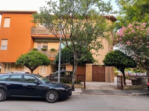 A residential street with a black car parked on the side, a tree in the foreground, and a building with a brown door and windows. - Modern Apartment Near Senigallia's Velvet Beach (Senigallia)
