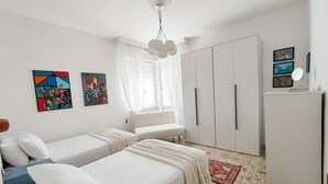 A bedroom with two beds, a wardrobe, a mirror, and artwork on the walls. - Modern Apartment Near Senigallia's Velvet Beach (Senigallia)