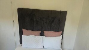 Una cama con cabecera oscura, almohadas blancas y rosadas, una manta rosa y una toalla blanca.