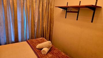 A room with a bed, a towel, a wall-mounted shelf, and a curtain.