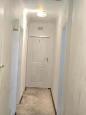A narrow hallway with a white door at the end, a light fixture above, and a carpeted floor. - Room-aquasaintsguest Lodge (Johannesburg)