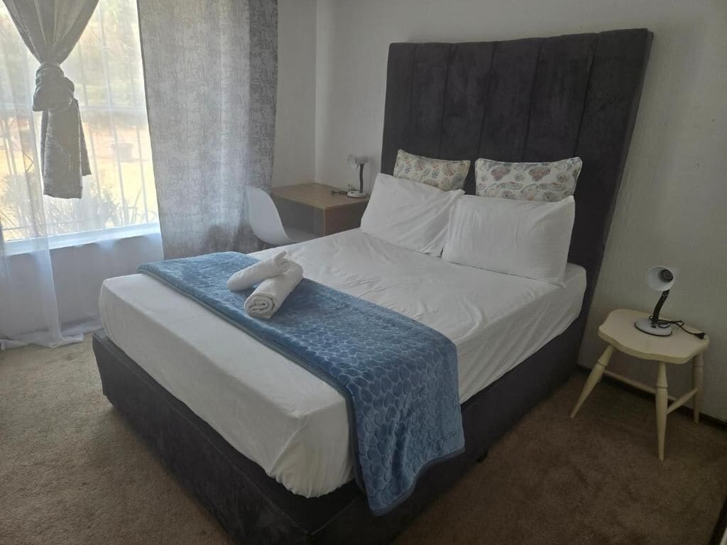 A bedroom with a bed, a bedside table, a lamp, and a window with curtains.