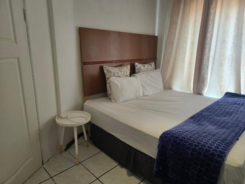 A hotel room with a bed, a small round table, and a window with curtains.