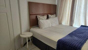 A hotel room with a bed, a small round table, and a window with curtains.
