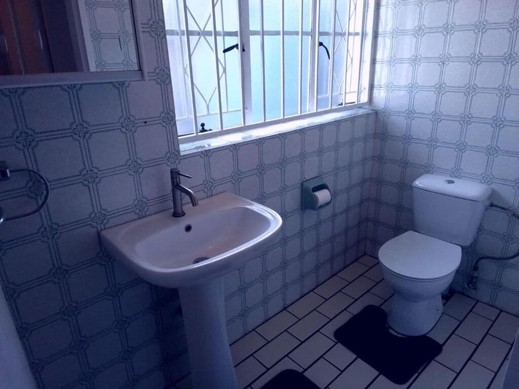 Une salle de bain avec un lavabo, des toilettes et une fenêtre avec des barreaux.