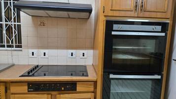 A kitchen with a built-in oven, a stove, and wooden cabinets.