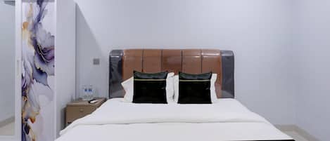A hotel room with a bed, a nightstand, a wardrobe, and a wall with a decorative panel.