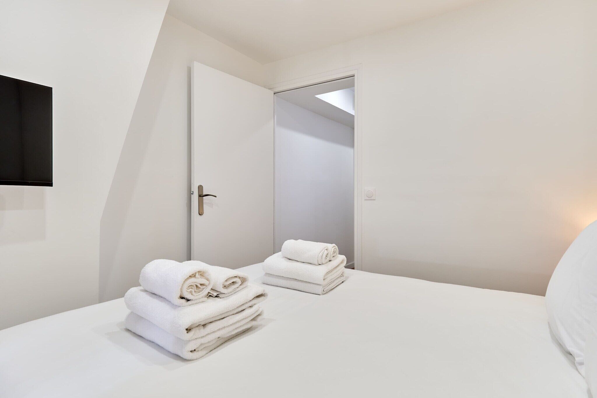 A hotel room with a bed, a door, and a wall-mounted light fixture.