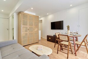 Ein modernes Wohnzimmer mit einer Couch, einem runden Couchtisch, einem Esstisch mit Stühlen und einem an der Wand befestigten Fernseher.