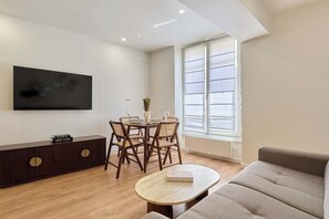 A modern living room with a flat-screen TV, a dining area with a table and chairs, a sofa, and a large window. - Apartment in the heart of the Marais (Paris)