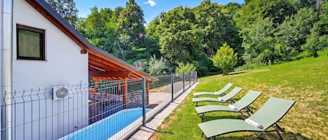 Una piscina con zona techada, césped y sillas de descanso.