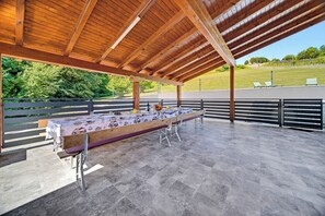 An outdoor covered patio area with a long table set for dining, surrounded by metal railings and a stone floor. - Greenwood Retreat With Hot Tub & Sauna (Sveti Martin na Muri)