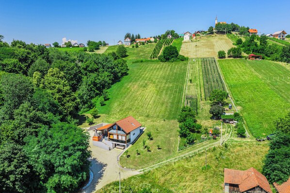 Ländliche Landschaft mit einem Haus auf einem Hügel, umgeben von Feldern und einer Kirche.