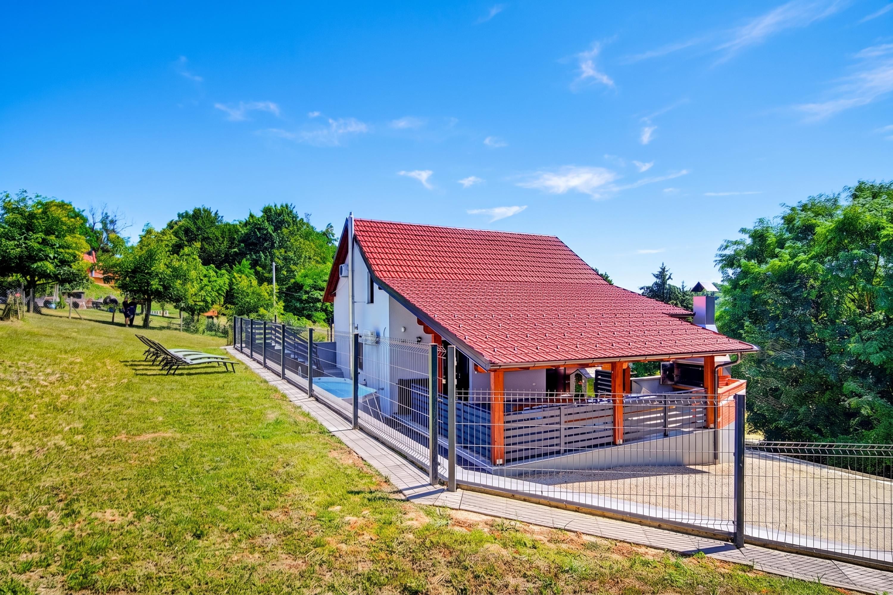 A modern house with a red roof, a swimming pool, and a fenced patio area.