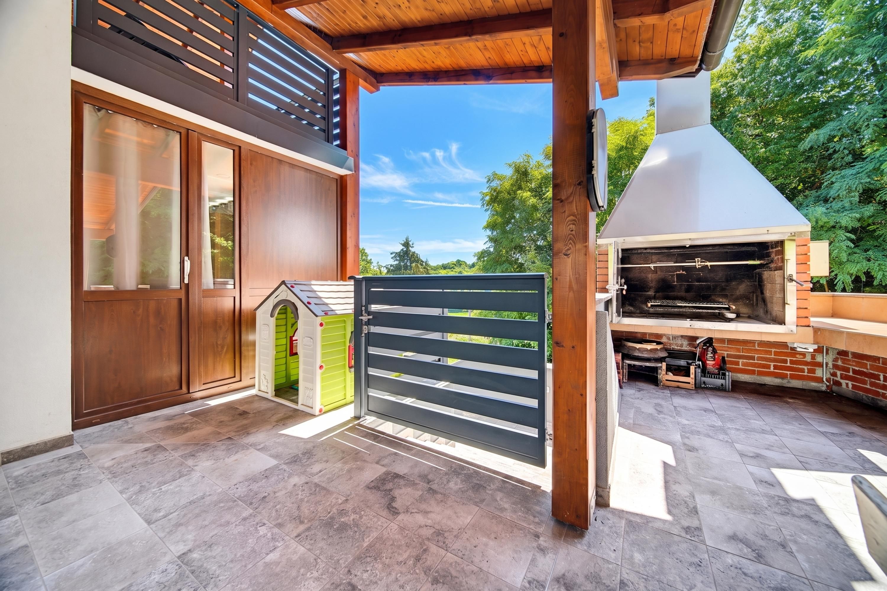 Une terrasse extérieure moderne, dotée d’un barbecue, d’une pergola en bois et d’une cabane de jeux verte.