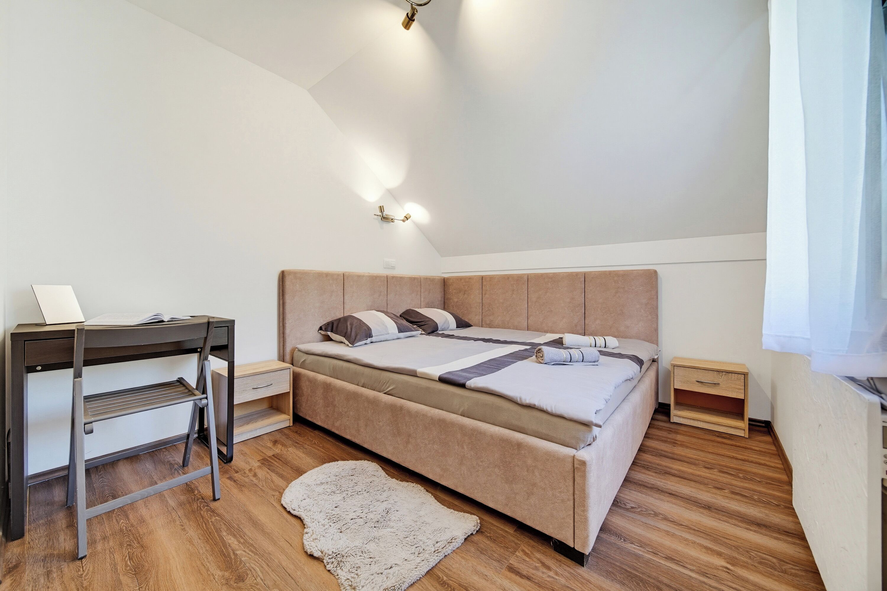 A bedroom with a bed, bedside tables, a desk, and a rug.