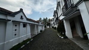 A narrow cobblestone street flanked by white buildings with balconies, under a cloudy sky. - Casa D'Ladera Bandung Deluxe Double Stay (Bandung)