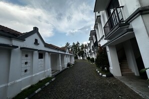 Eine enge Kopfsteinpflasterstraße, gesäumt von weißen Gebäuden mit Balkonen, unter einem bewölkten Himmel.