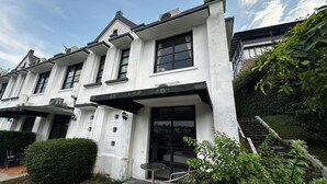 A white building with a front entrance, a small outdoor seating area, and a staircase leading to an upper level. - Casa D'Ladera Bandung Deluxe Double Stay (Bandung)