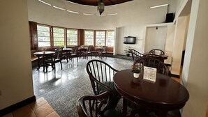 Comedor con mesas y sillas redondas, ventanas amplias y un ventilador de techo.