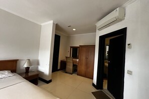Habitación de hotel con cama, mesita de noche, lámpara, armario y unidad de aire acondicionado.