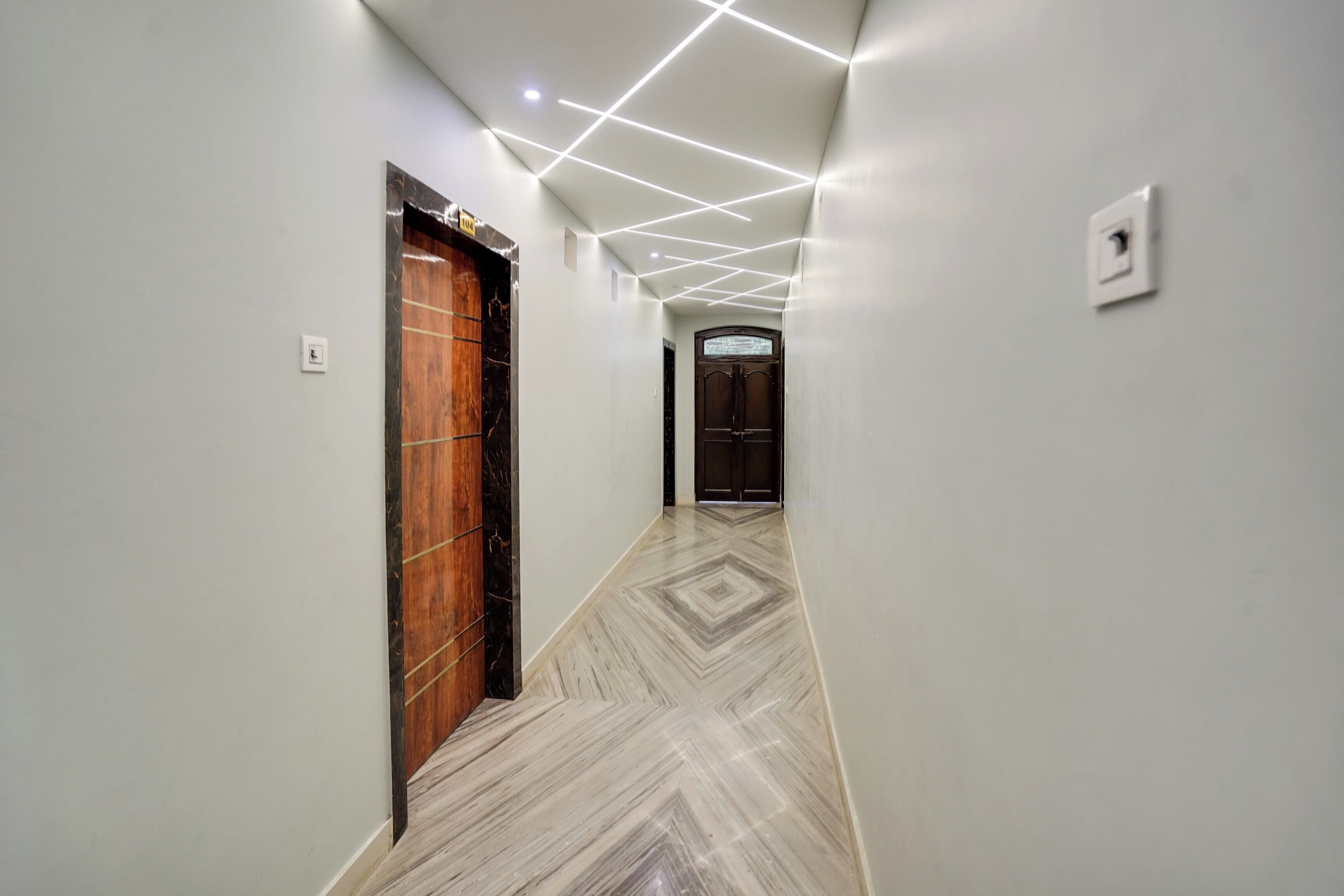 Un pasillo con una puerta de madera, una puerta negra e interruptor de luz en la pared.