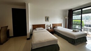 Habitación de hotel con dos camas, una mesita de noche con lámpara, un cuadro en la pared y una ventana con vistas.