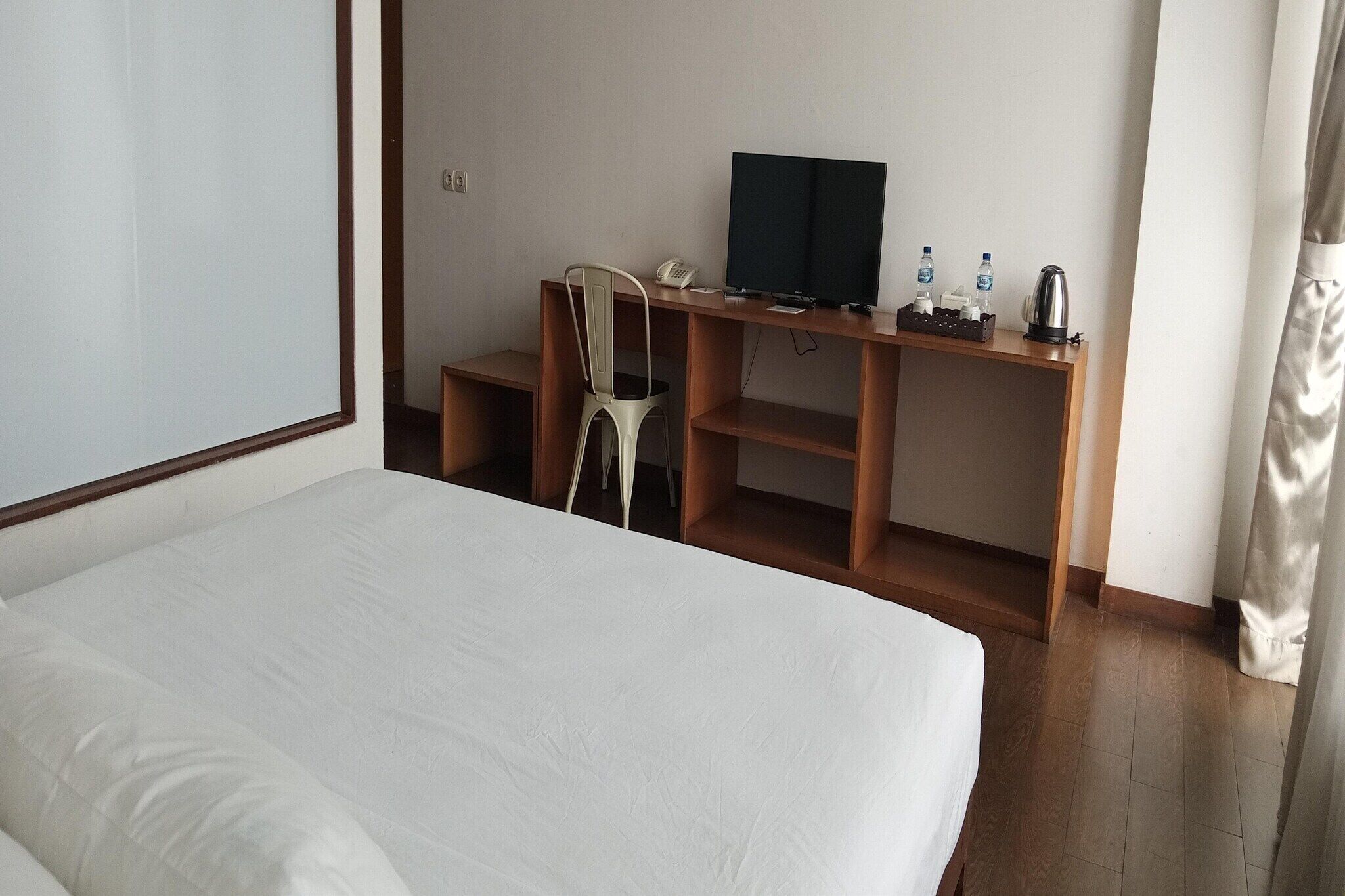 A hotel room with a bed, a desk with a television, a chair, and a telephone.