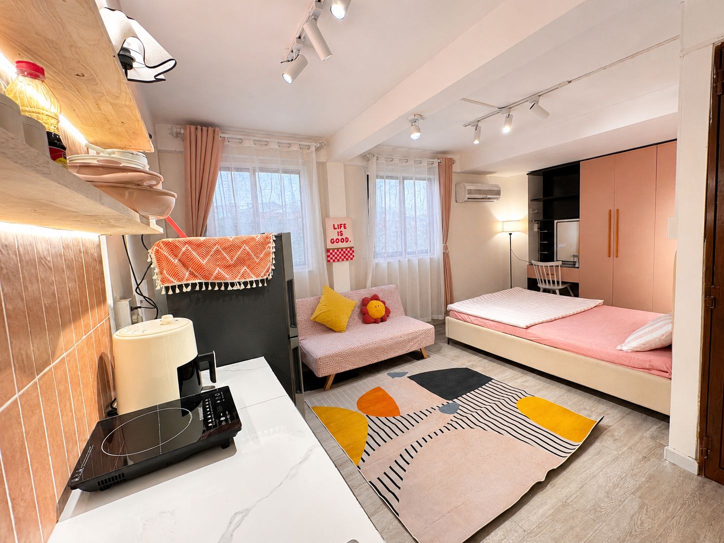 Ein modernes Schlafzimmer mit einem Bett, einem Schreibtisch mit einem Laptop, einem Stuhl und einem kleinen Tisch mit einer Flasche.