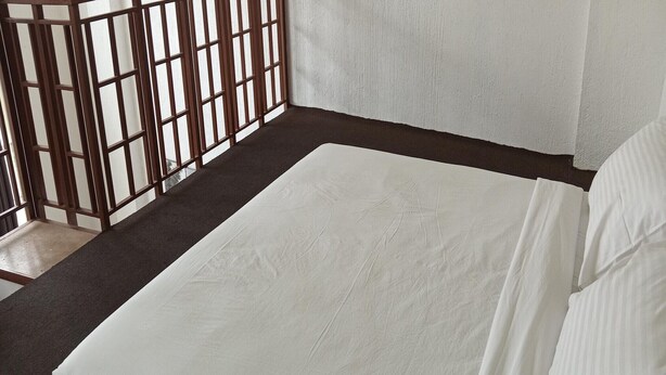 Una habitación con una cama, un separador de madera y una pared con textura.