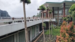Un edificio moderno con un paseo techado, plantas en macetas y vistas a una edificación distante.