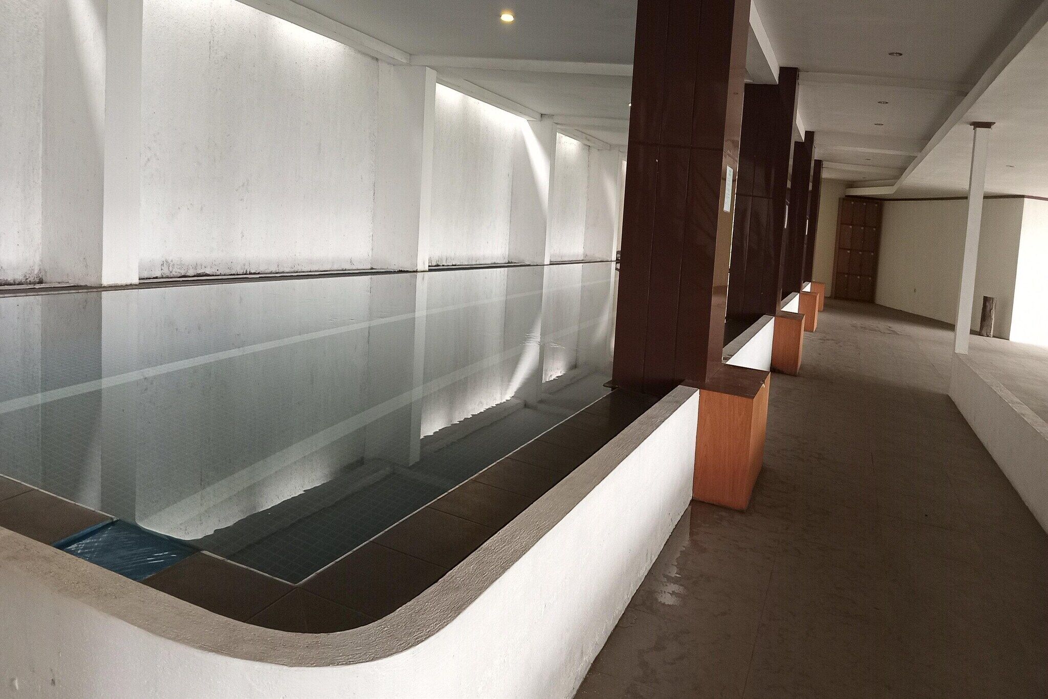 A corridor with a reflective glass partition, wooden columns, and a tiled floor.