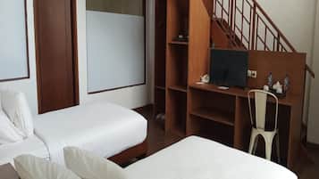 A hotel room with two single beds, a wooden desk with a computer, a chair, and a staircase.
